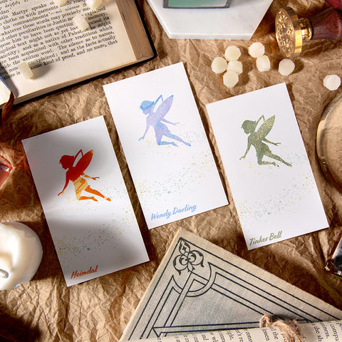 Wearingeul Tinker Bell Ink Swatch Cards, depicting fairy silhouettes on 200gsm paper, surrounded by stationery and books. 50-card pack ideal for fountain pen ink enthusiasts.
