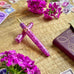 Esterbrook Estie - Punch / Gold - Techo Custom Nib fountain pen, marbled lavender-pink resin with gold trim, surrounded by magenta flowers and a burgundy leather notebook in a still-life setting.