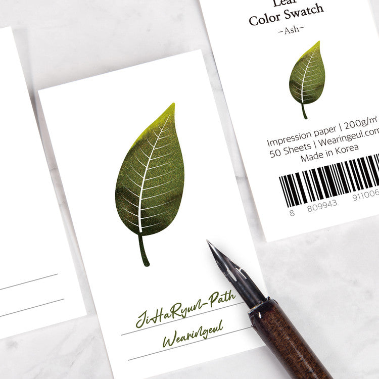 Wearingeul Ash Leaf Ink Swatch Cards on marble, showcasing a stylized green leaf design. Includes fountain pen nib. 50-sheet pack, 200gsm Impression paper, enhancing ink characteristics.
