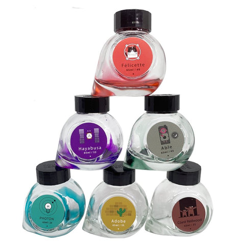 Six stacked Colorverse Empty Bottles, each 65ml, with black lids and unique labels, offering a random selection supporting charitable donations.