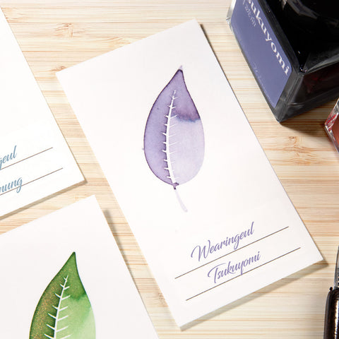 Wearingeul Ash Leaf Ink Swatch Cards on display, featuring watercolor leaf designs and an ink bottle, showcasing fountain pen ink characteristics on smooth, 200gsm paper.
