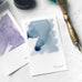 Wearingeul Instant Film Colour Swatch (50 sheets) on marble, featuring abstract watercolor cards and brass dip-pen. Ideal for fountain pen ink shading and sheen testing.