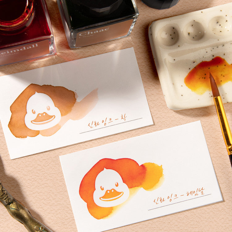 Wearingeul White Duck Ink Swatch Cards with cartoon duck silhouettes, surrounded by ink washes, displayed with glass ink bottles and drawing tools on a wooden surface.