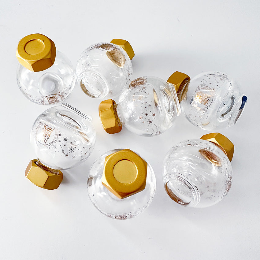FWP (20ml) Empty Ink Bottle by Ferris Wheel Press features a clear glass body with gold starbursts and a hexagonal brass cap, ideal for fountain pen ink enthusiasts.