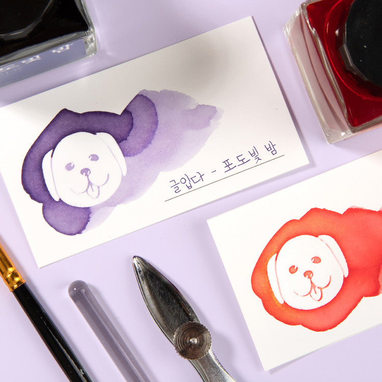 Wearingeul White Puppy Ink Swatch Cards with smiling dog illustrations, ink bottles, and tools on a lilac surface. Ideal for showcasing fountain pen ink properties.