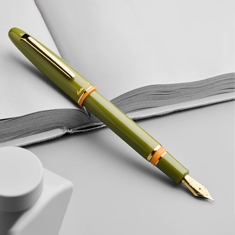 Esterbrook Estie fountain pen in Quirky Leaf with gold accents on an open notebook, showcasing its medium nib, embodying 1970s retro charm and modern functionality.