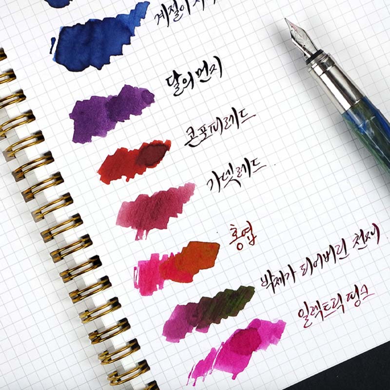 Wearingeul Reservoir Ring Note - A5 (Grid) with ink swatches and a marbled fountain pen, showcasing fountain pen-friendly graph paper in a minimalist, spiral-bound notebook.