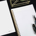 Wearingeul Reservoir Ring Note - A5 (Grid) notebook with gold spiral binding and fountain pen friendly grid pages, alongside a fountain pen on a minimalist desk setup.