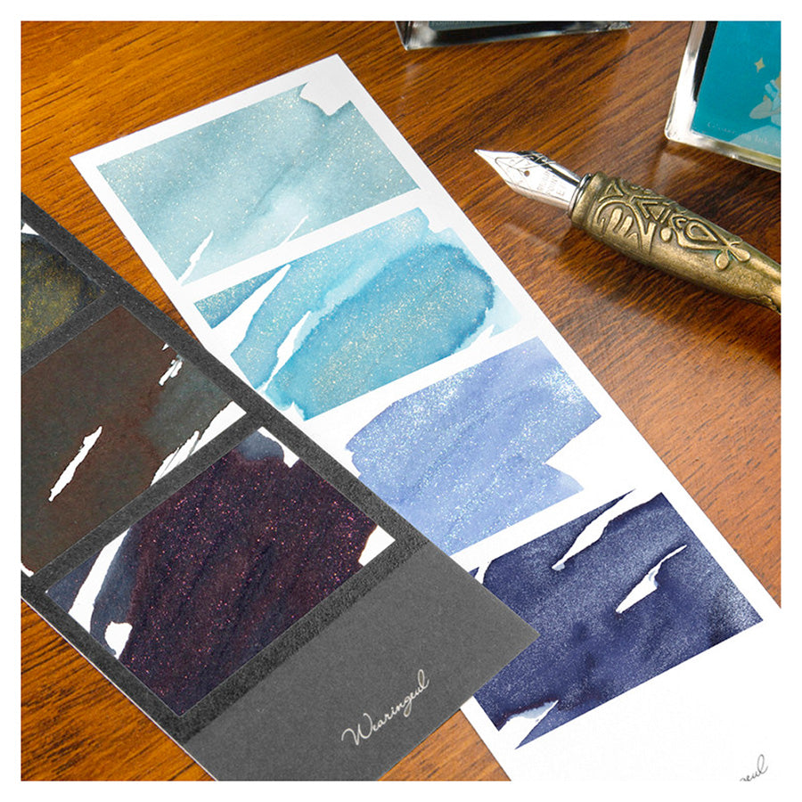Wearingeul Four Photos Color Swatch (30 Sheets, White) with shimmering ink swatches and a brass-handled fountain pen nib on a wooden surface. Ideal for fountain pen ink testing.