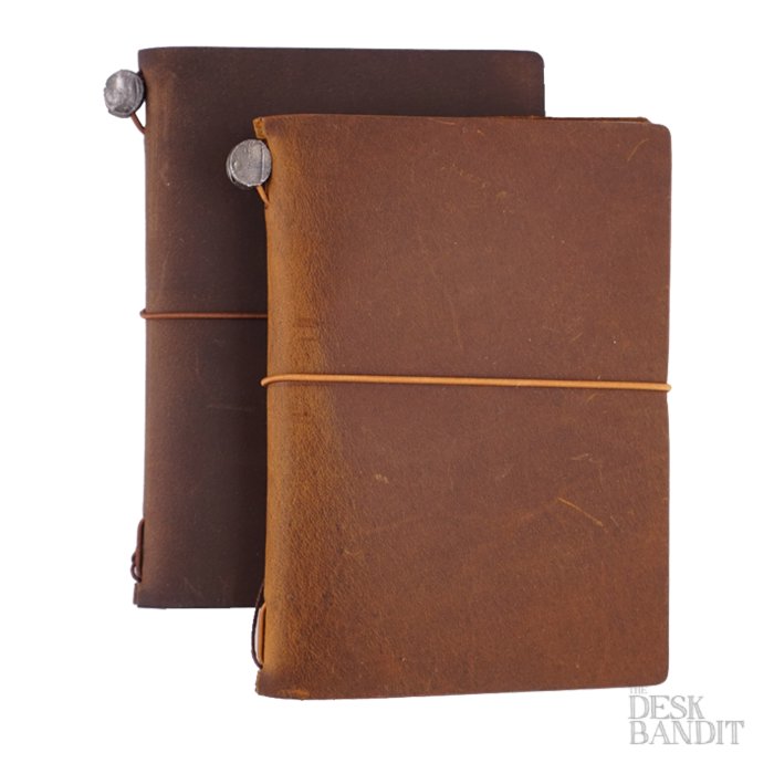 Two rustic Passport Leather Covers (Brown) with elastic closures and metal buttons, featuring a The Desk Bandit logo. Includes a blank notebook and cotton pouch.