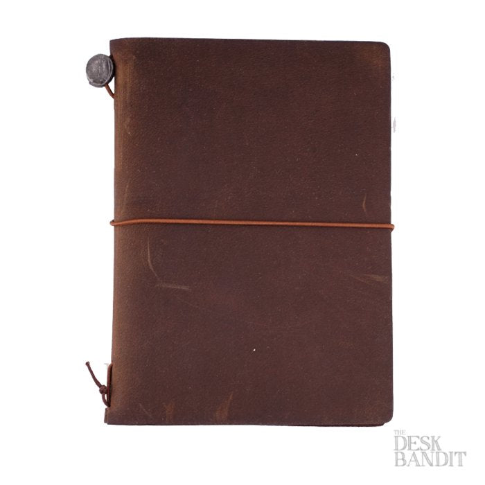 Passport Leather Cover (Brown), a dark-brown leather journal with a metal button and elastic closure, featuring a The Desk Bandit logo in the corner.