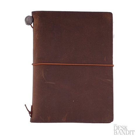 Passport Leather Cover (Brown), a dark-brown leather journal with a metal button and elastic closure, featuring a The Desk Bandit logo in the corner.