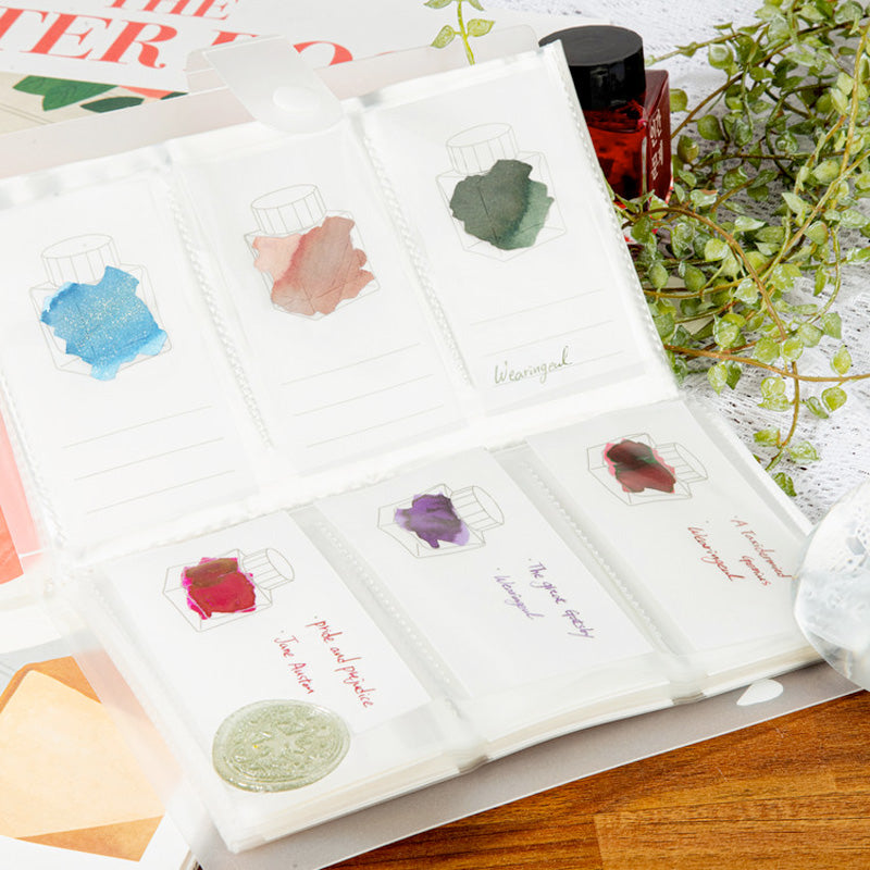 Wearingeul Tracing Ink Swatch Cards (Vertical) in a ring-bound folder with diverse ink samples, surrounded by a red ink bottle and decorative elements on a wooden table.