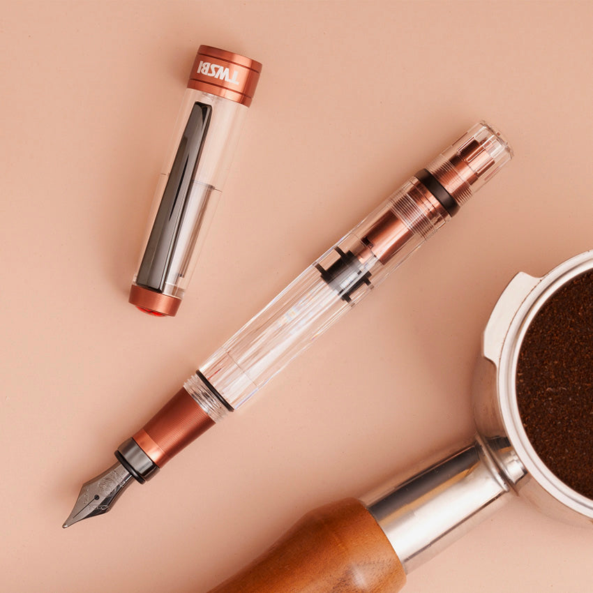 Diamond 580 ALR (Affogato with Onyx) fountain pen, featuring a clear barrel, copper grip, and stub 1.1 nib, beside espresso portafilter with ground coffee.