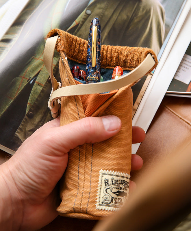 Esterbrook 2GO Cup (British Tan) pen pouch held in hand, showcasing a leather strap closure and fountain pens, including a blue-and-gold marbled cap, nestled inside.