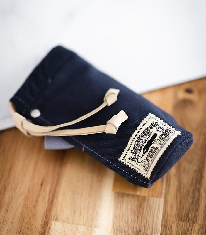 Esterbrook 2GO Cup (Navy Blue) with leather drawstring and vintage logo, perfect for carrying fountain pens, featured on a wooden surface.