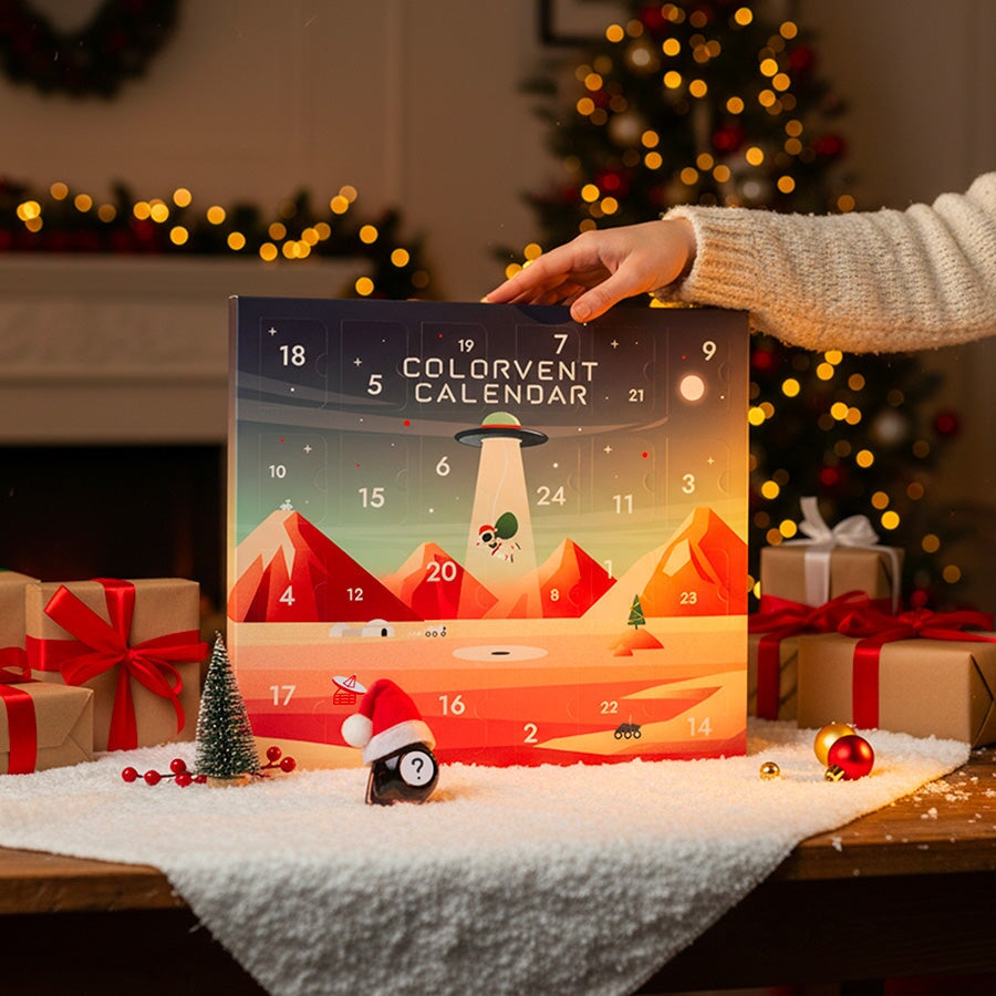 2025 Colorvent Calendar featuring 24 fountain pen inks, displayed amid festive decor including gift boxes, a tabletop tree, and a penguin figurine.