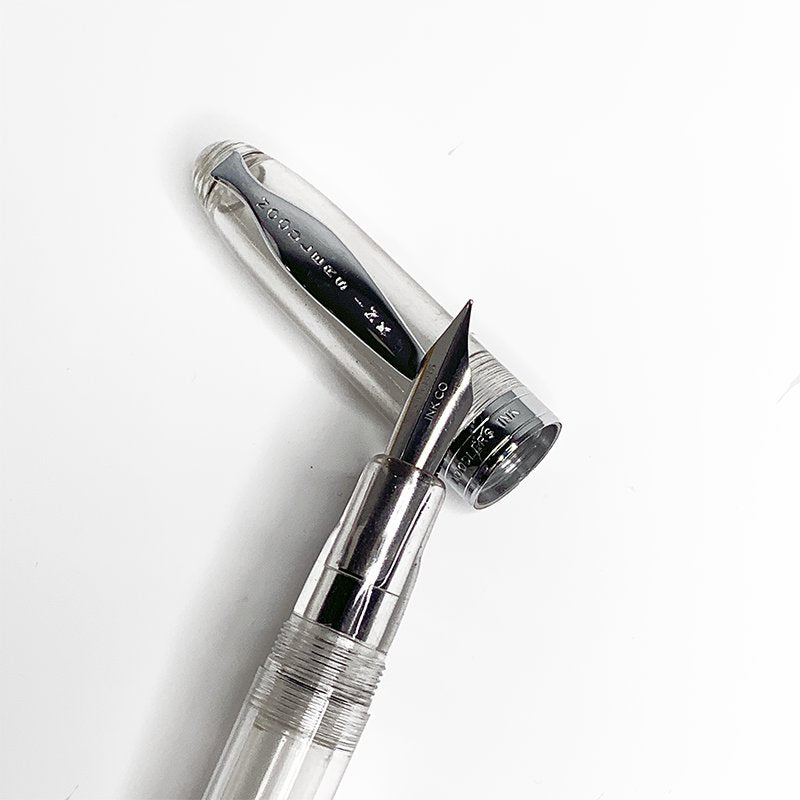 Ahab Flex - Clear Demonstrator fountain pen with exposed flexible steel nib and transparent barrel, alongside its shiny metal cap, showcasing versatile filling options.