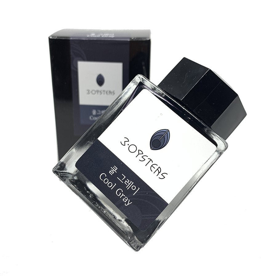 Tilted square glass bottle of 3OYSTERS Cool Gray ink, featuring a black cap and white label, stands before its matching box.