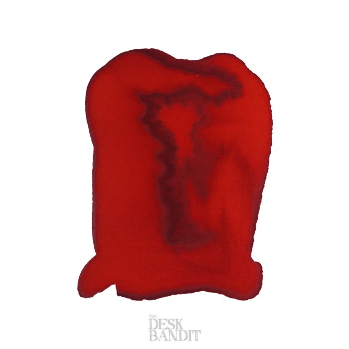 Close-up swatch of Robert Oster's Fire Engine Red - 2ml ink, showing a deep center with feathered edges and a subtle Desk Bandit watermark.