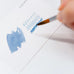 Close-up of a hand testing Colorverse Ink Swatch Cards - Size B (Plain) with blue fountain pen ink, showcasing solid washes and loops on premium Nebula 200gsm paper.