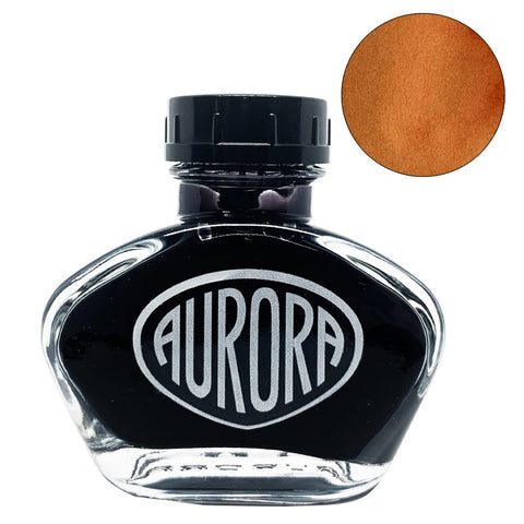 Aurora 100th Anniversary - Orange (55ml) inkwell, featuring a glass body with a black screw cap, showcases a sepia/amber ink swatch in the upper-right corner.