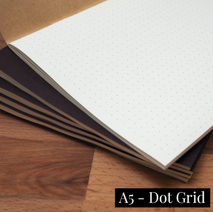 Tomoe River Insert - A5 Dot Grid, shown open on a wooden surface, revealing its dot-grid pages. Stacked with similar notebooks, highlighting its slim, portable design.