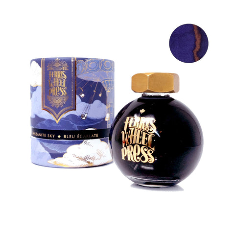 Tanzanite Sky - 85ml: Round glass ink bottle with gold cap, blue-purple box with fairground motifs, and a rich blue ink swatch with coppery-red sheen.