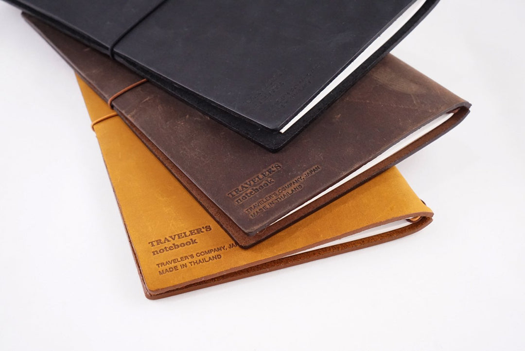 Leather Cover (Brown) atop a stack of mustard and black covers, each with a white paper insert, showcasing Traveler&