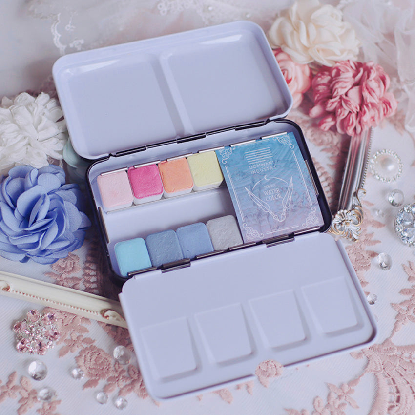 Fantasy of Rococo Watercolor Set by Dominant Industry displayed open with pastel half-pan colors on lace, surrounded by vintage-inspired decor, ideal for creative desk setups.